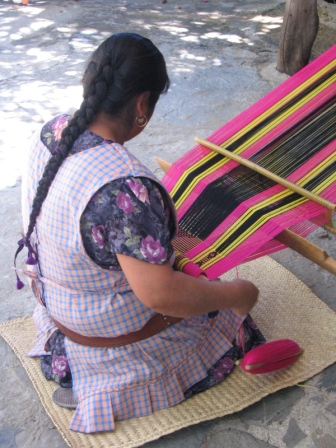 Zapotec woman weaving table runner on a backstrap loom at home workshop.